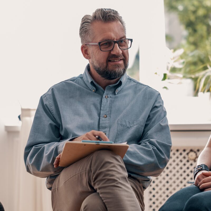 Smiling man talking with friends during meeting for teenagers with therapist