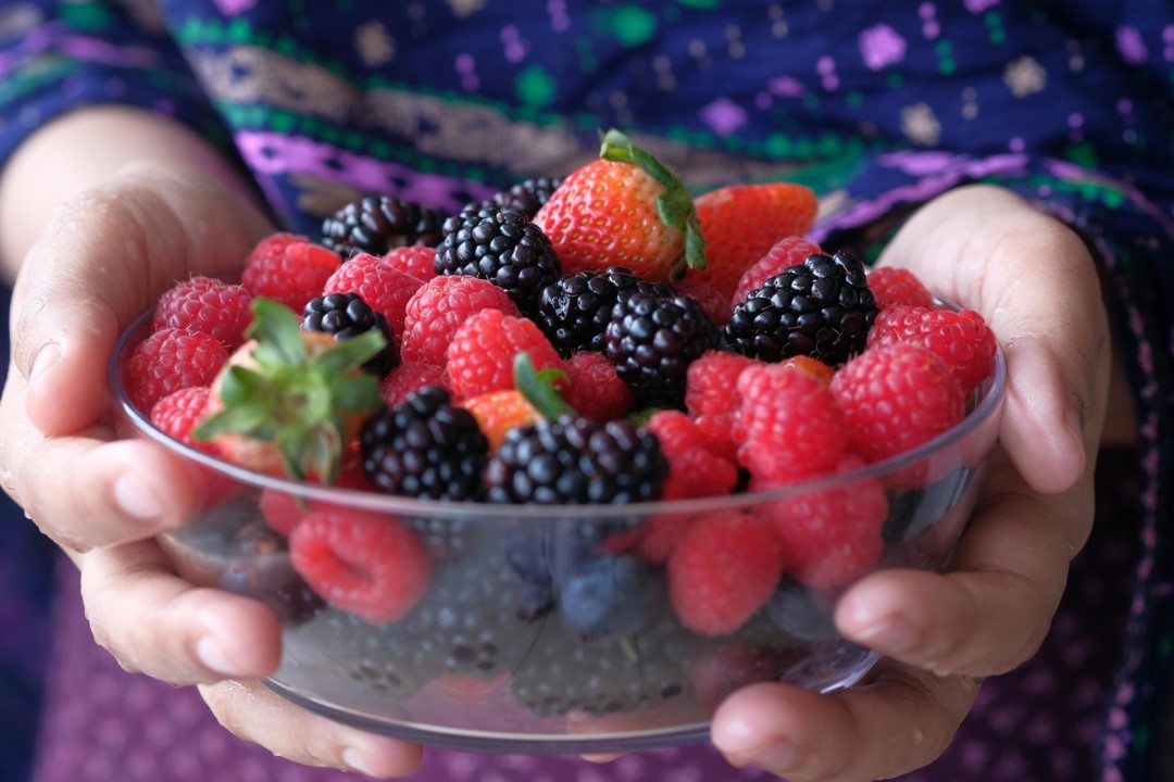 Child hands holding a glass bowl of strawberries, blackberries